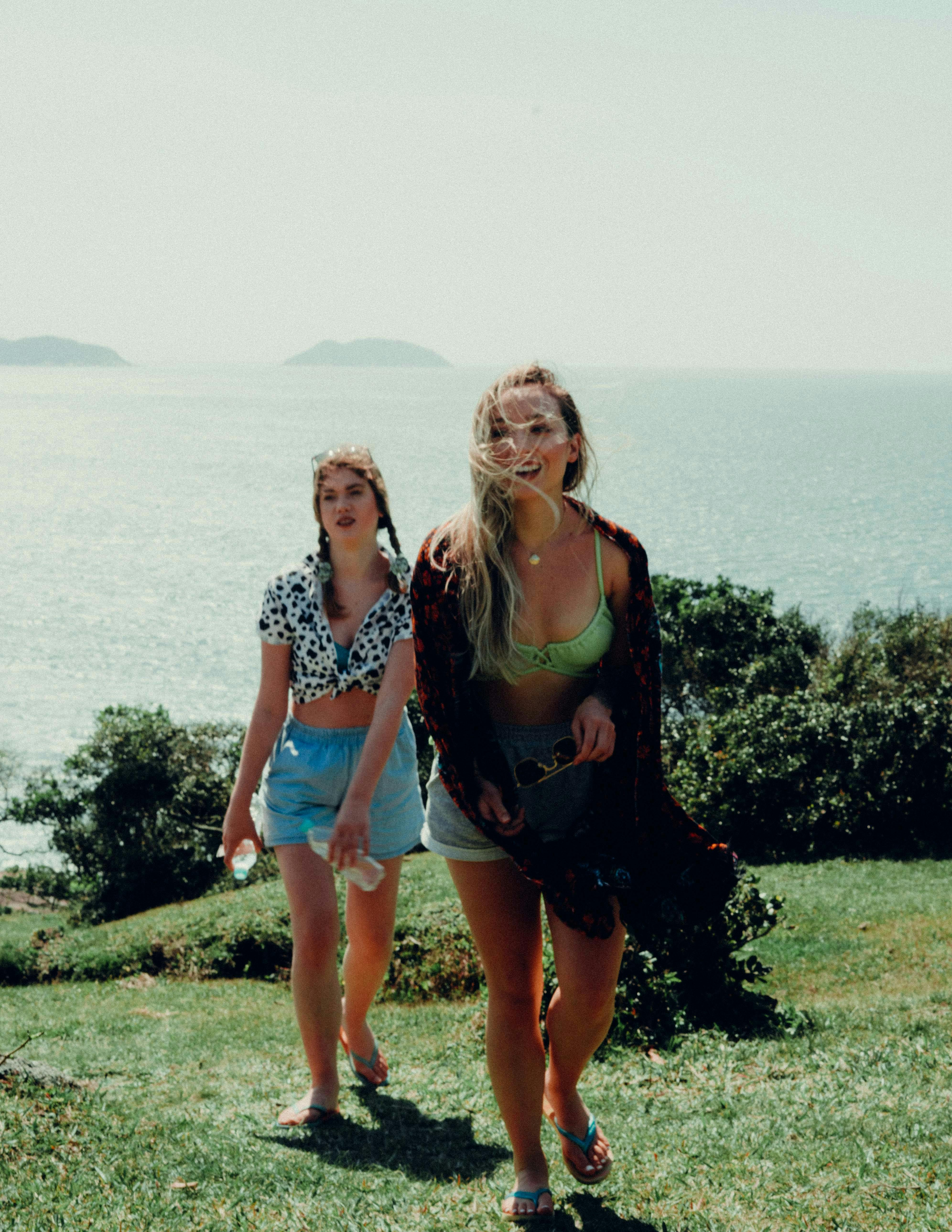 Two women exploring a scenic grassy cliff overlooking the ocean on a sunny day.