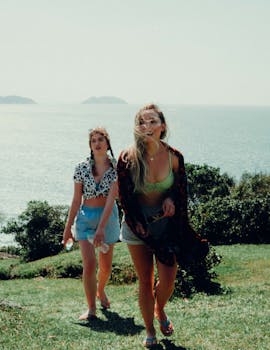 Two women exploring a scenic grassy cliff overlooking the ocean on a sunny day.