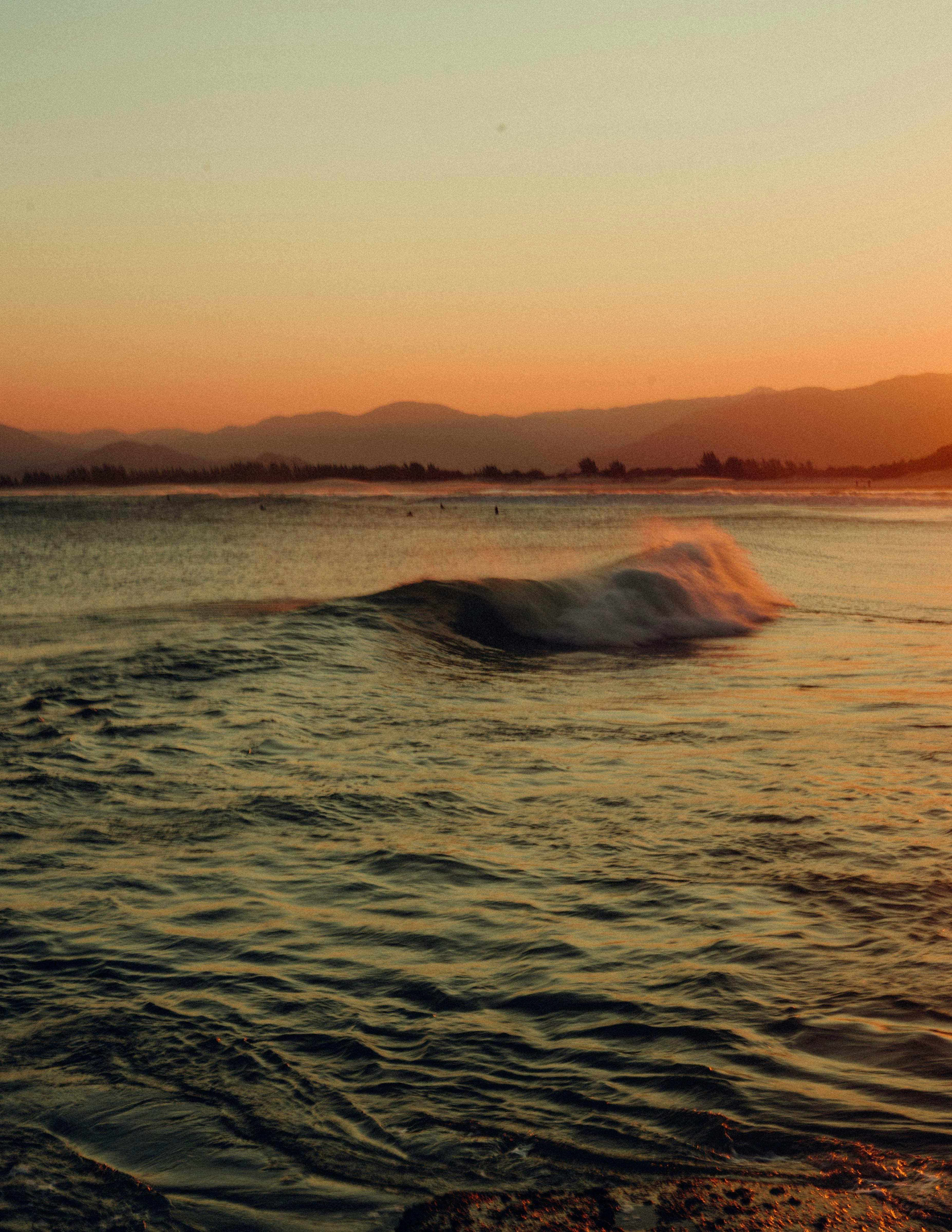 Tranquil ocean waves with a mountain backdrop under a vibrant sunset sky.