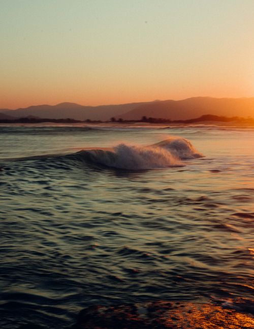 Free Breathtaking view of ocean waves at sunset with mountains in the background, capturing serene beauty. Stock Photo