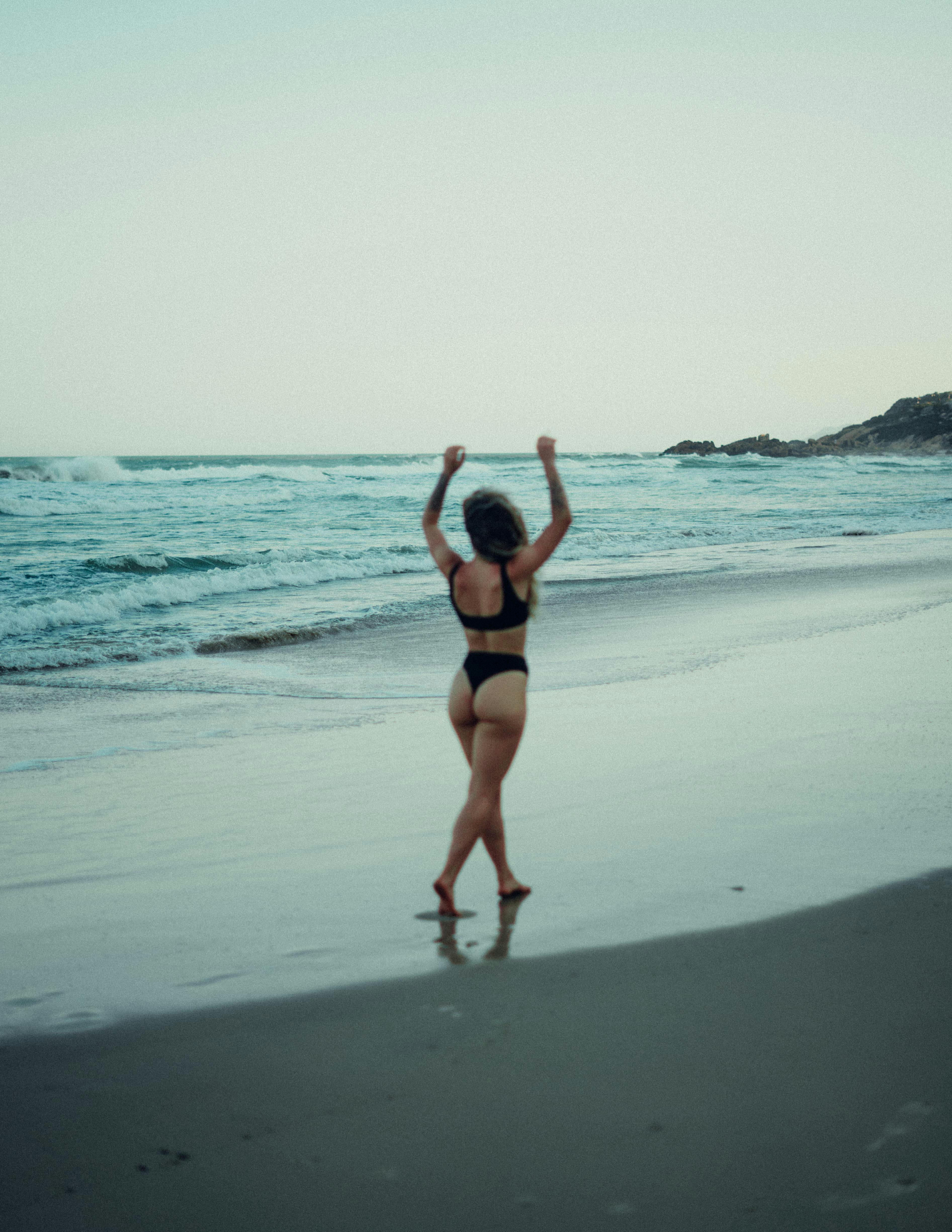 A woman enjoying a peaceful and carefree walk along the beach at daybreak, embracing the ocean breeze.