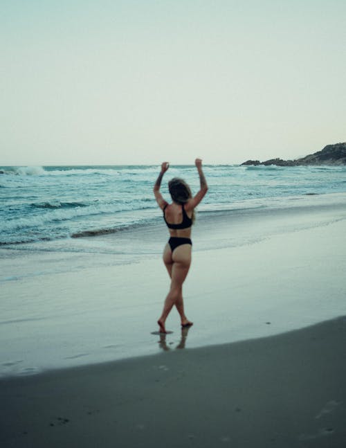 Free Woman in Black Bikini Walking on Seashore Stock Photo