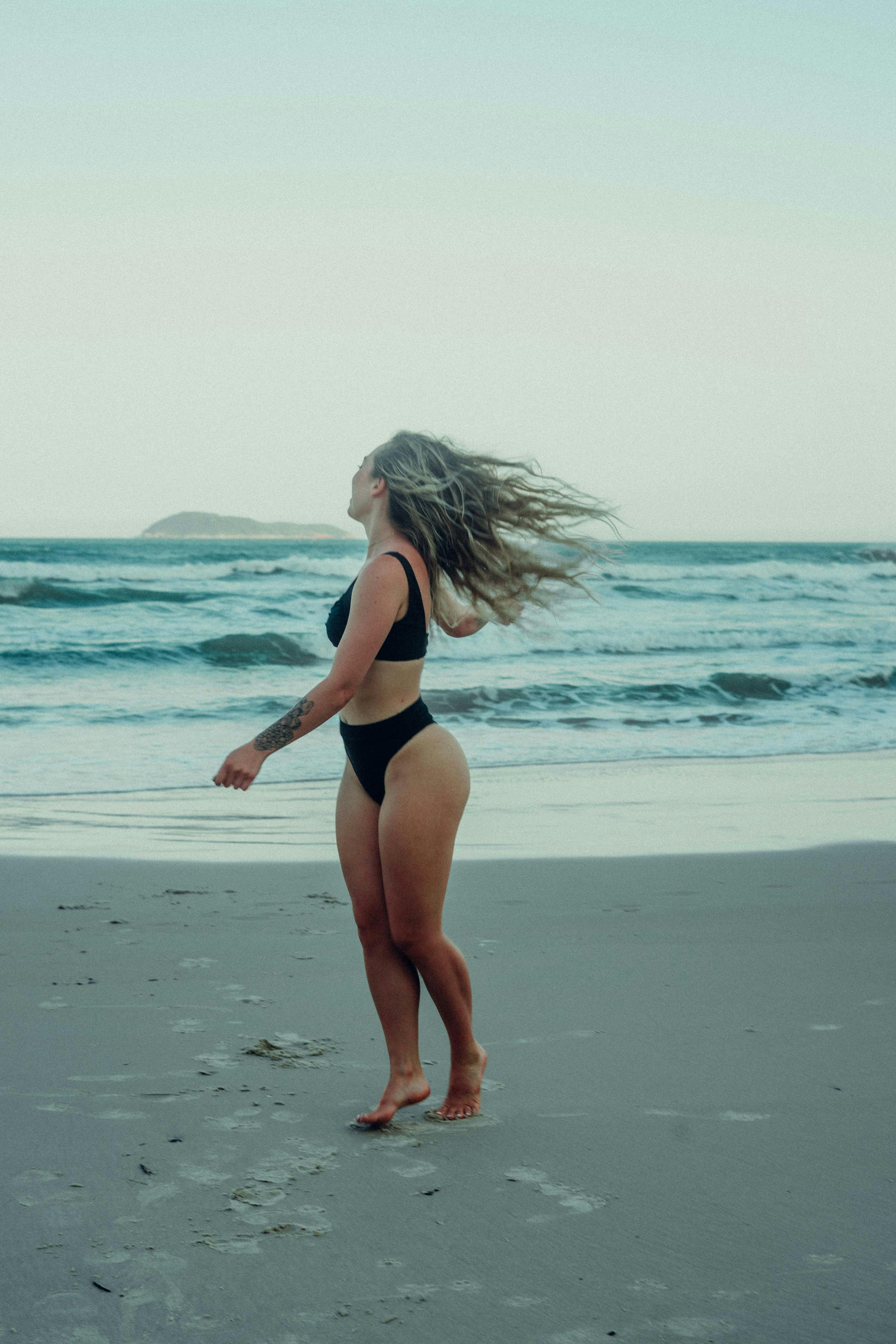 woman in black bikini with flying hair on beach