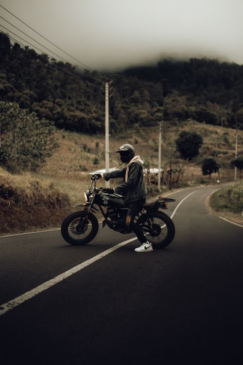 Free Motorcyclist riding through lush green mountains on a winding road. Perfect for travel and adventure visuals. Stock Photo