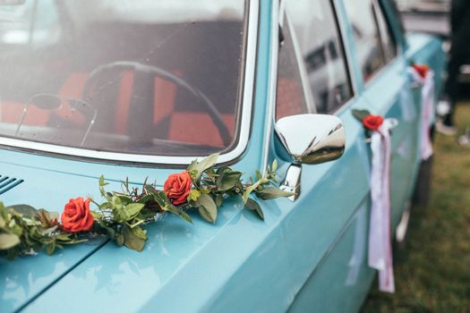 A classic blue car adorned with red roses and greenery, perfect for a wedding.