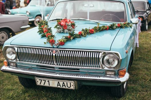 A classic blue car adorned with a floral garland, showcasing vintage elegance outdoors.