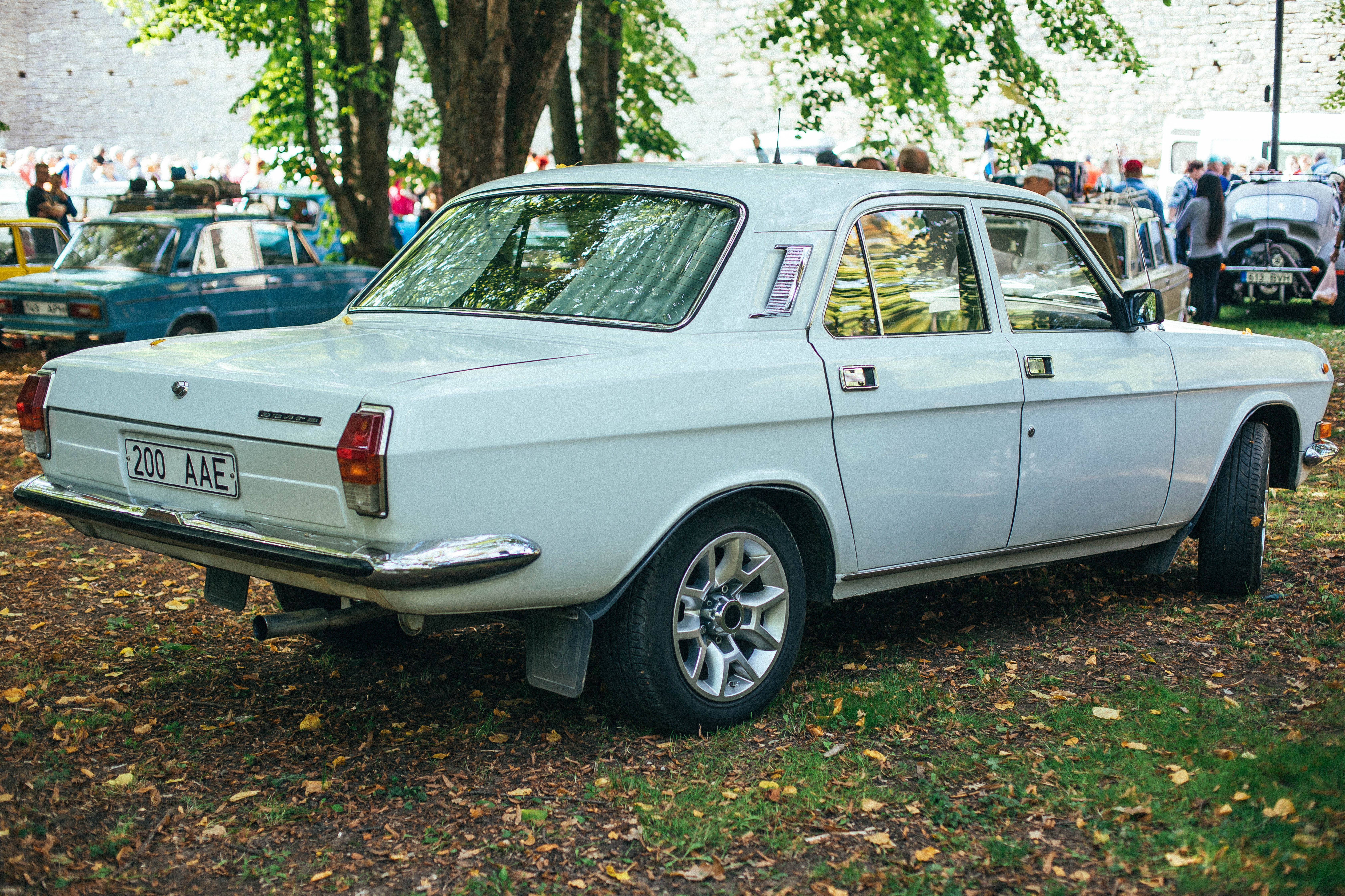 A classic vintage car displayed at an outdoor auto show under tree shade.