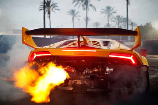 A powerful yellow sports car emitting flames, set against palm trees, creating a thrilling atmosphere.