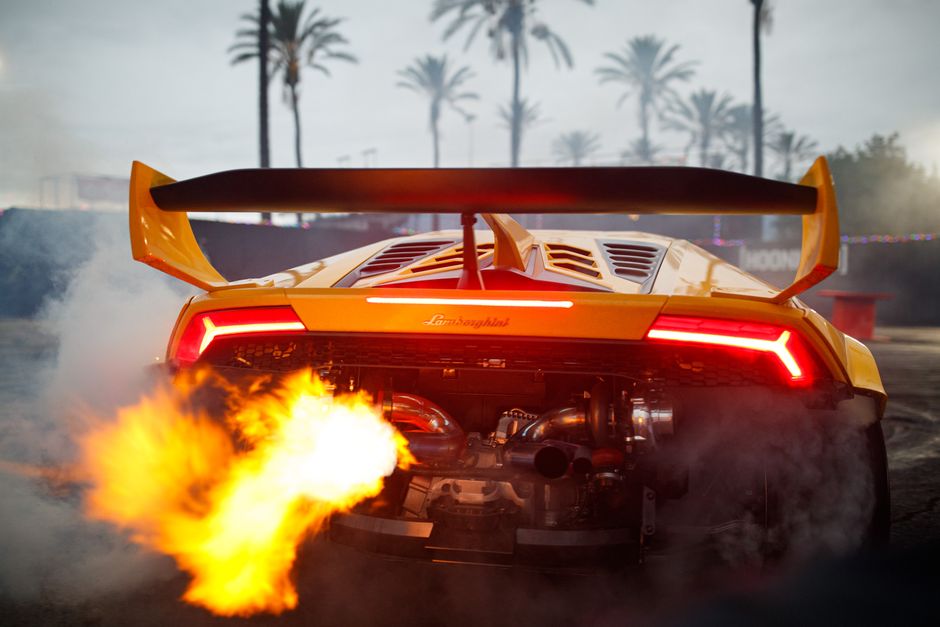 A powerful yellow sports car emitting flames, set against palm trees, creating a thrilling atmosphere.