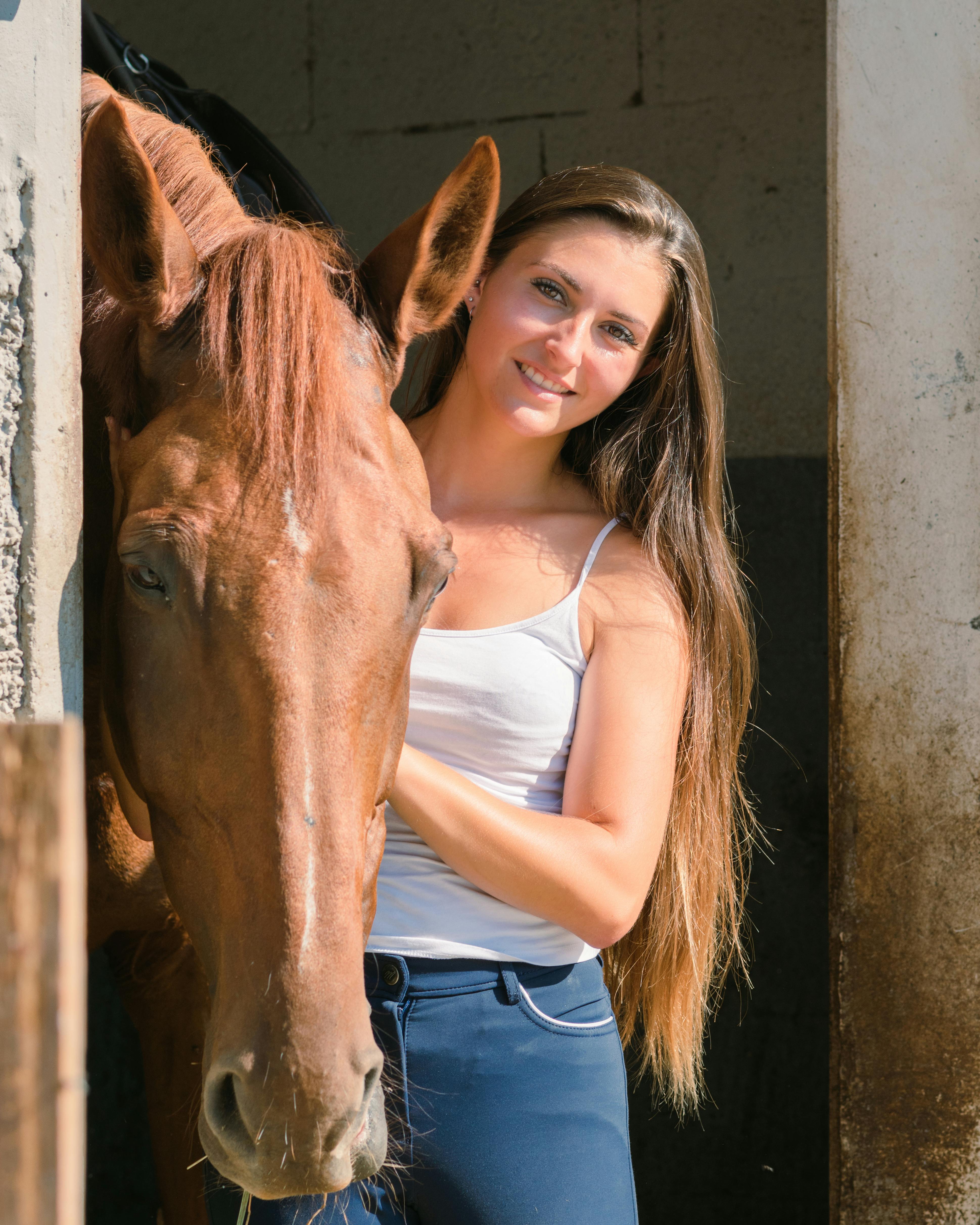 A woman standing beside a horse at the stable entrance, sharing a gentle moment.