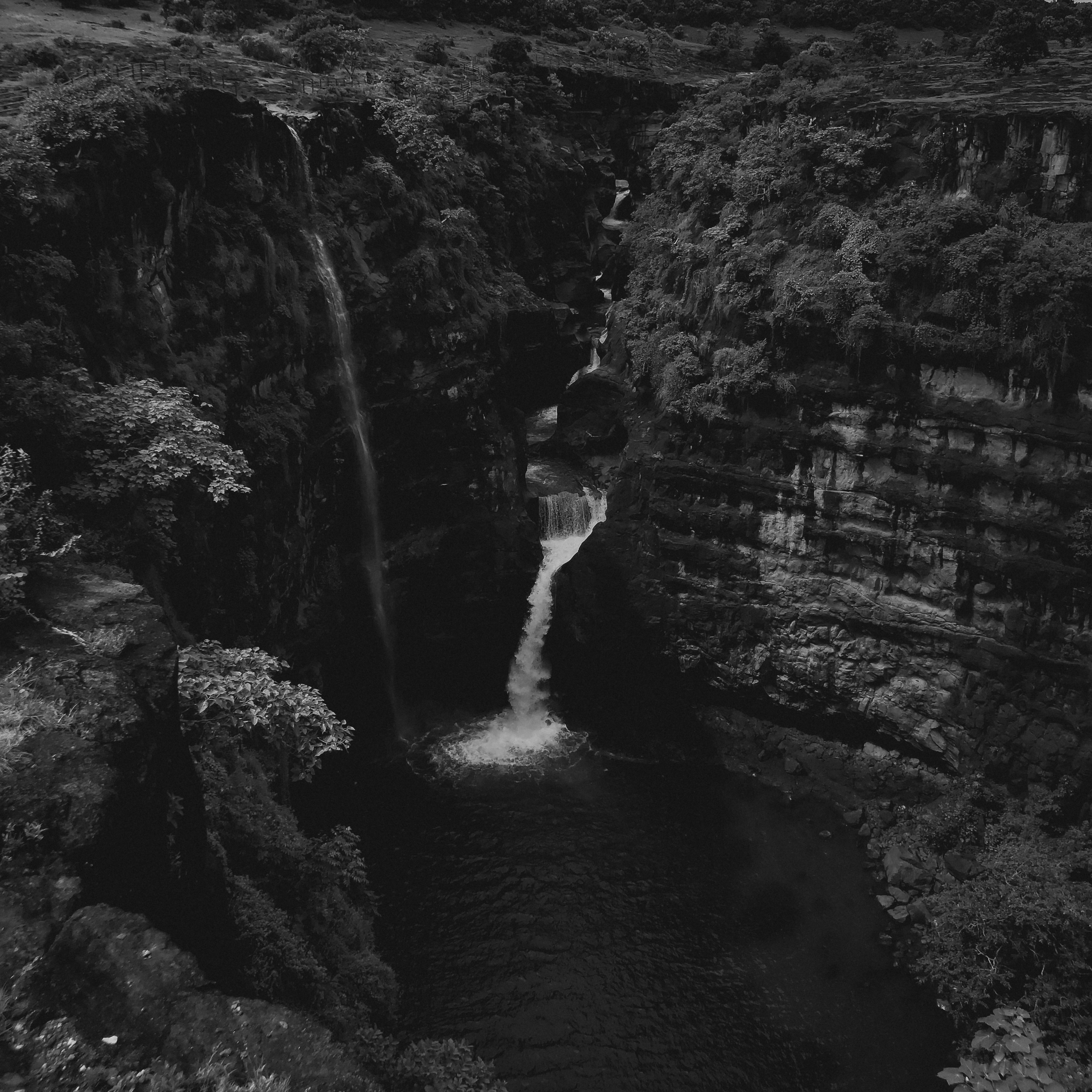 An aerial shot capturing a dramatic monochrome waterfall surrounded by rugged cliffs.