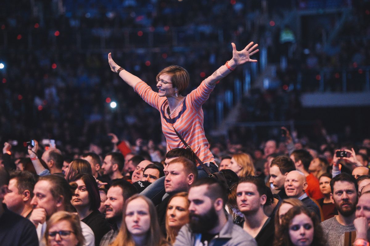 Large event audience with arms raised in a packed arena