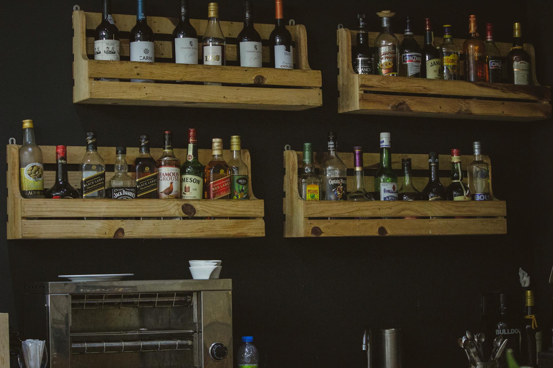 A rustic wooden shelf display of liquor bottles on a dark wall, perfect for a bar setting.