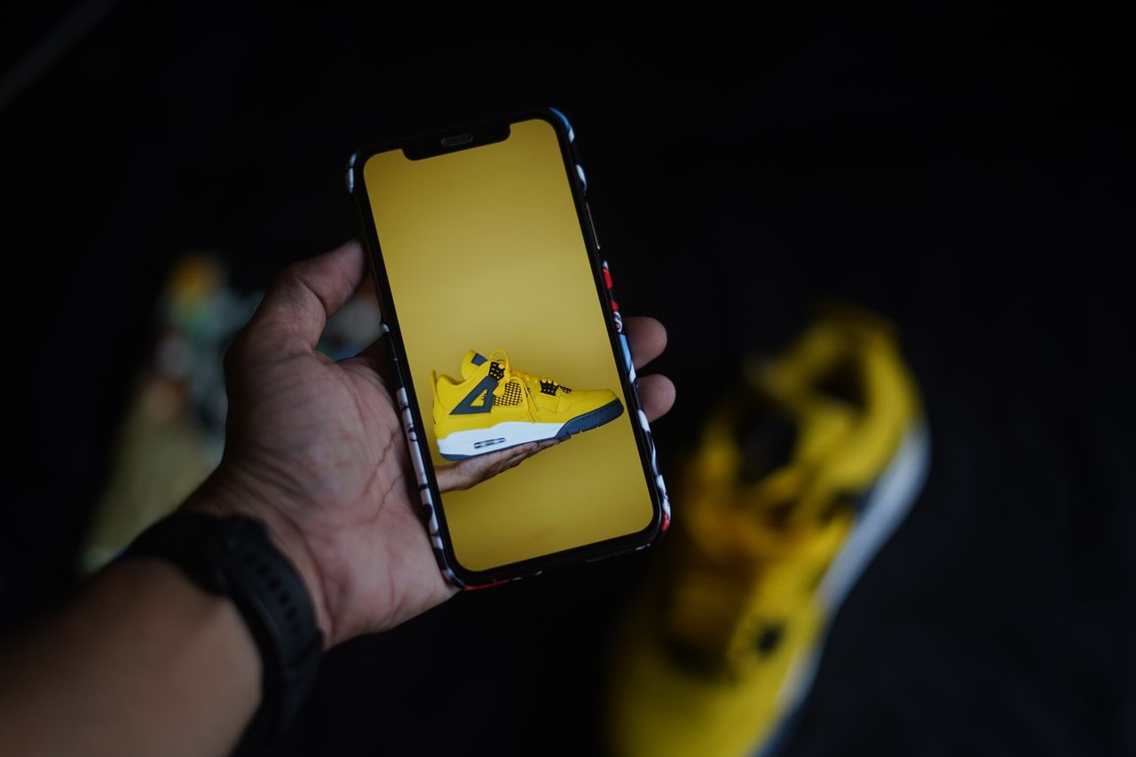 hand holding smartphone showcasing a yellow sneaker against a dark bac