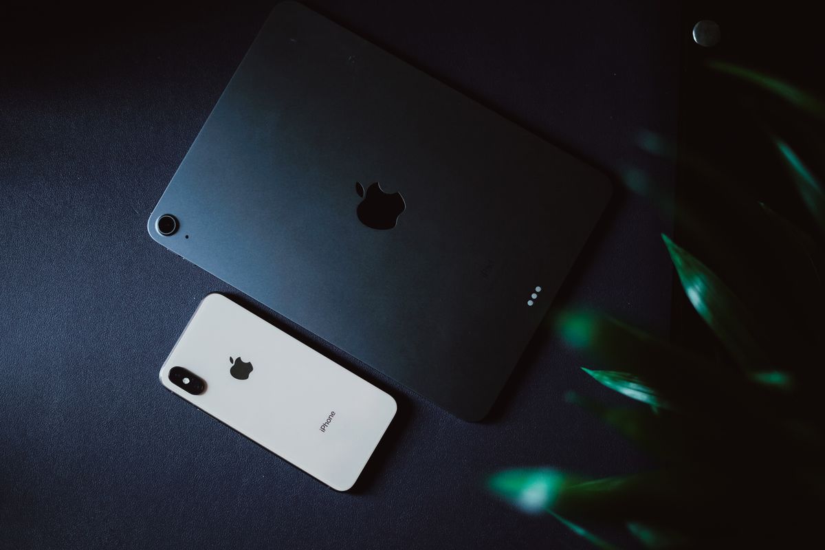 Modern gadgets including an iPhone and iPad placed on a black surface with a moody aesthetic.