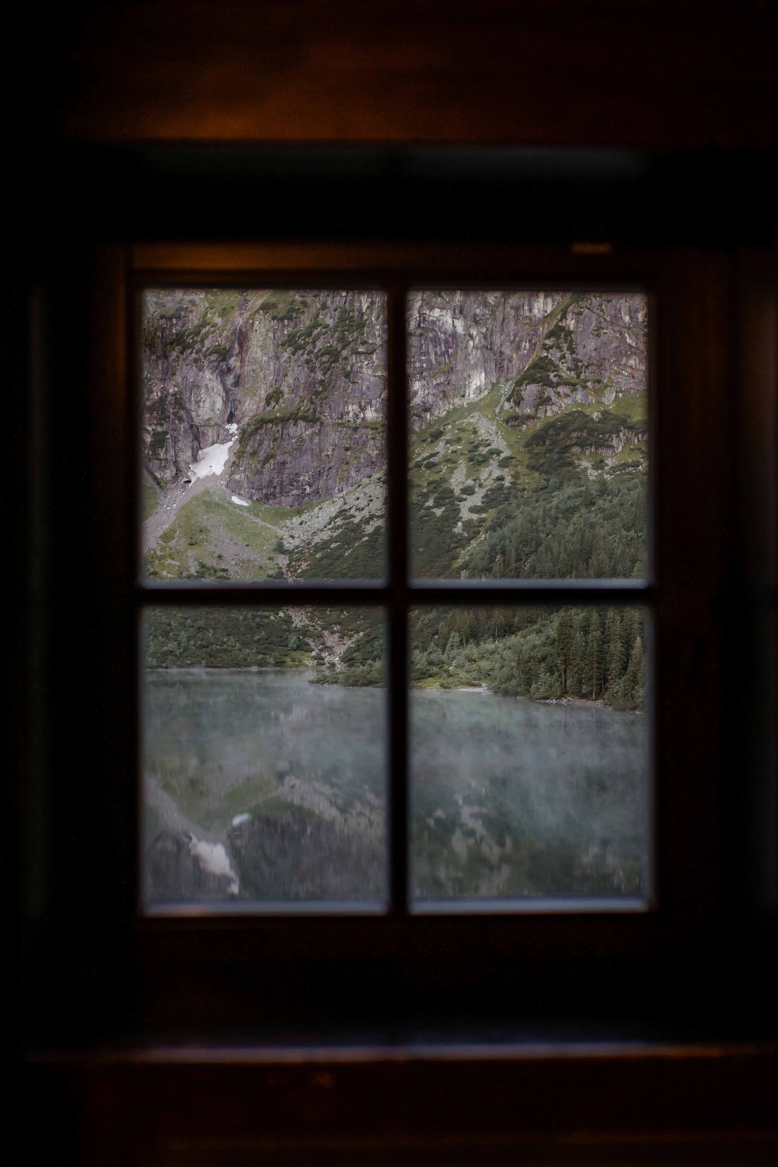 Peaceful lake and mountain scenery through a rustic window frame.