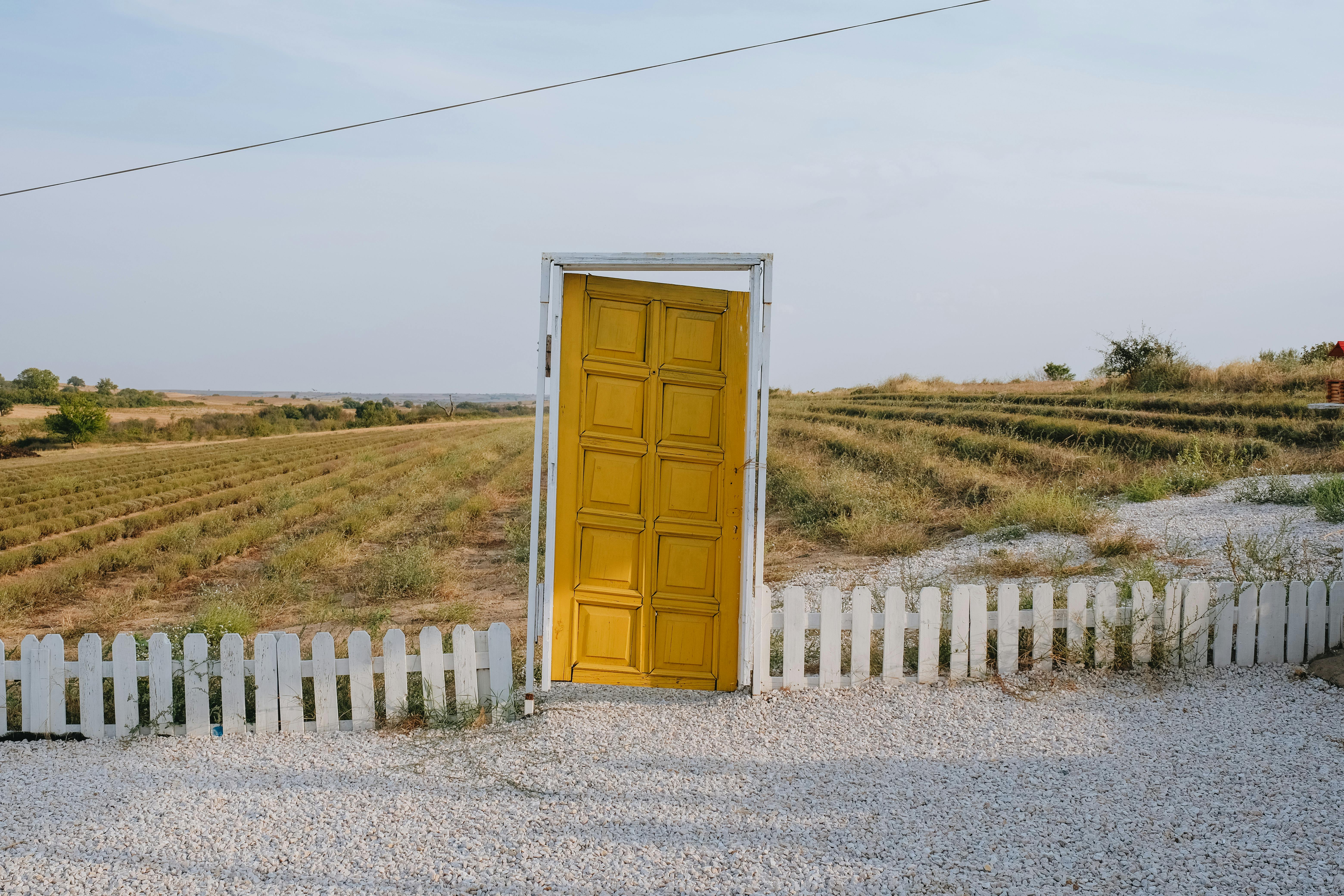 A unique yellow door stands amid a rural field, creating a surreal landscape scene.