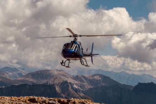 Free Blue helicopter flying over breathtaking mountain landscape with dramatic clouds in the sky. Stock Photo