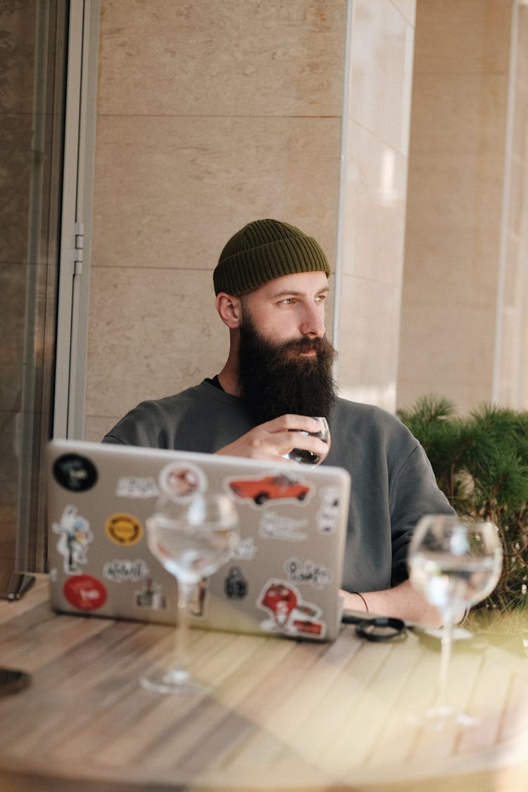 Thoughtful Bearded Man Using Laptop And Holding Glass Of Wine