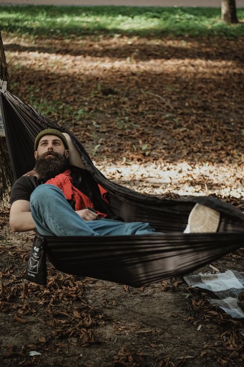 Free Casual shot of a bearded man resting in a hammock under trees, showcasing leisure and relaxation. Stock Photo