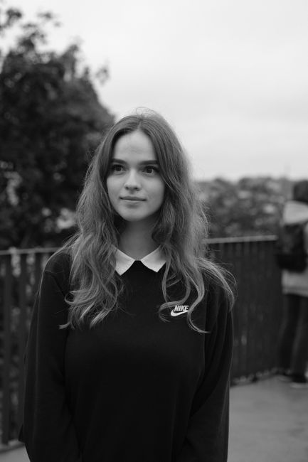 Black and white of smiling young female with long wavy hair in black sweatshirt standing in park and looking away