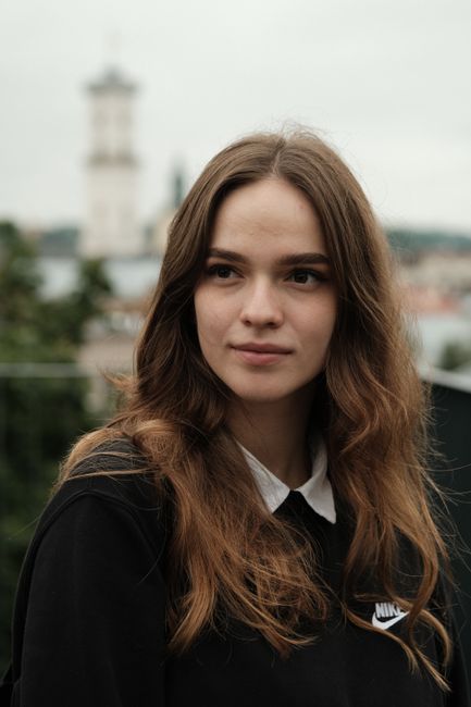 Close-up portrait of a young brunette woman with a blurred cityscape background.