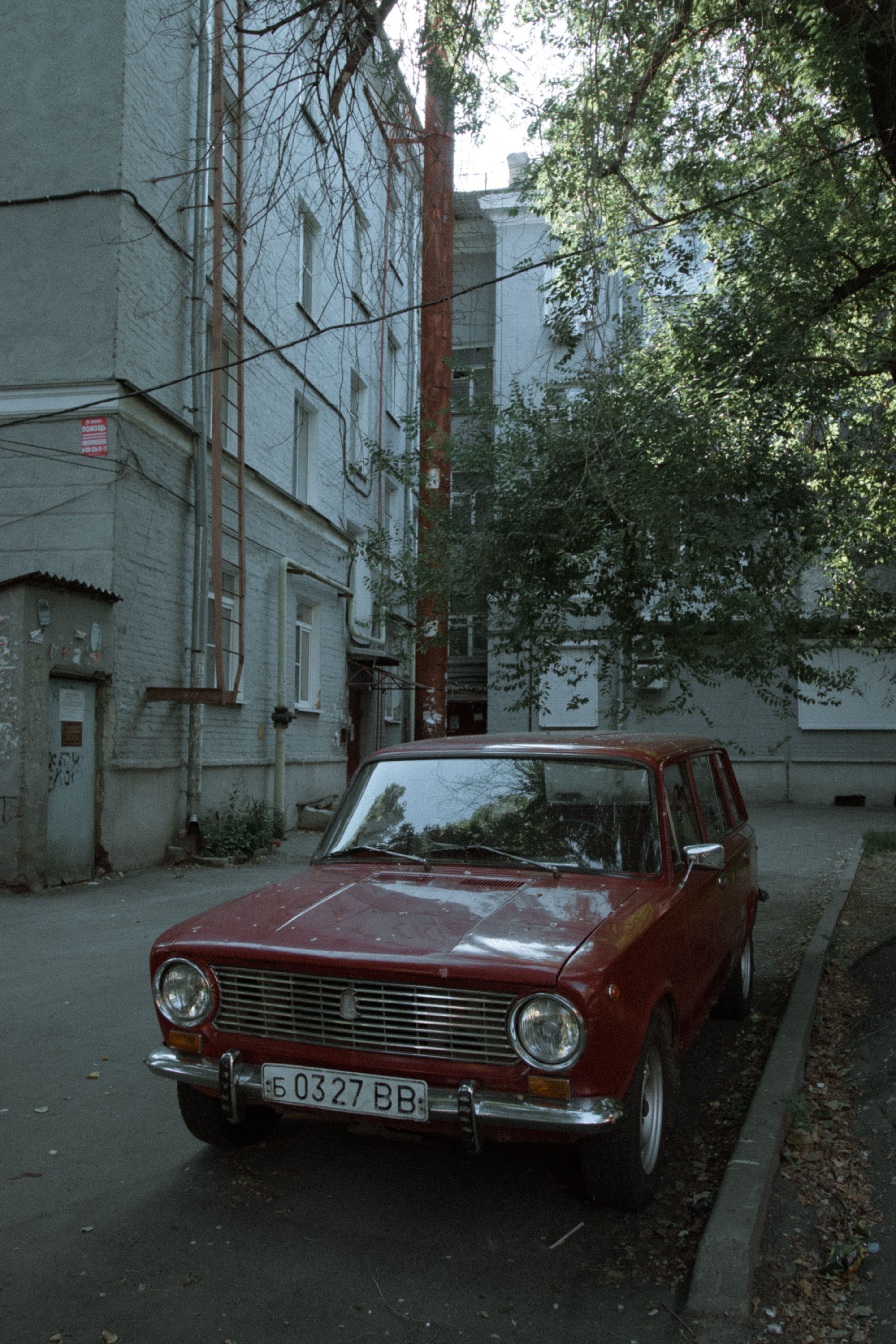 Red vintage car parked by the building in a quiet urban street.