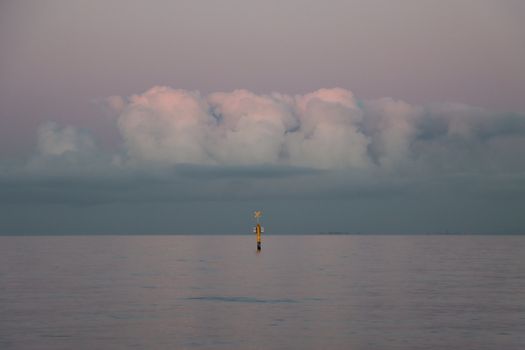 Tranquil seascape featuring a navigation buoy at dawn under dramatic clouds.