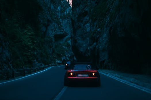 A car traverses a narrow road through a dramatic rocky mountain pass at dusk.