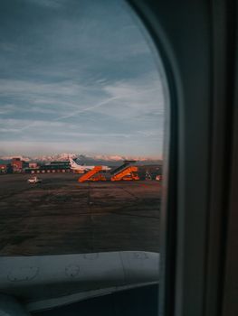 View from airplane window at sunrise, showing a plane and snowy mountains.