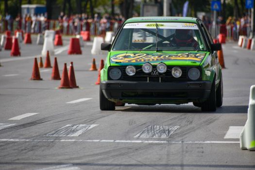 A vibrant green race car maneuvers through traffic cones on a city street during a racing event.