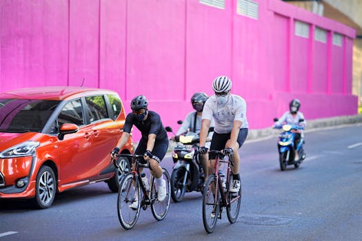 Two cyclists biking through Jakarta's streets with vibrant pink backdrop and urban traffic.