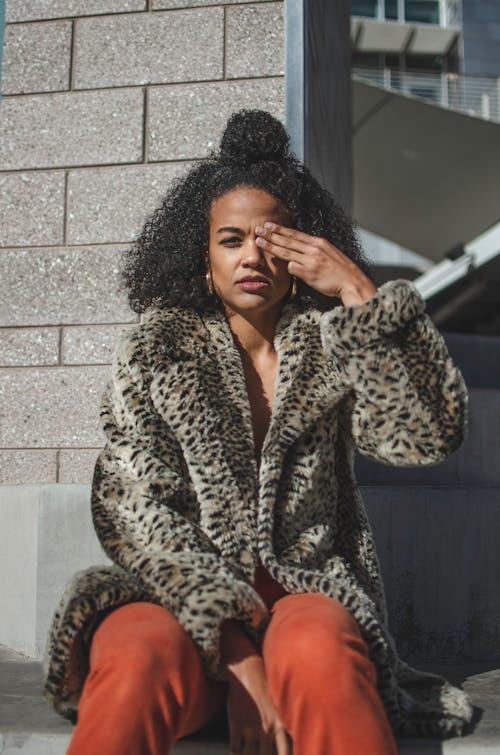 A Woman in Leopard Print Coat Sitting while Covering Her Eye Using Her Fingers