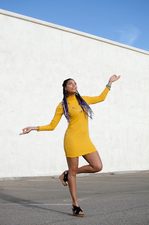 A Woman in Yellow Dress Standing on One Leg while Looking Up