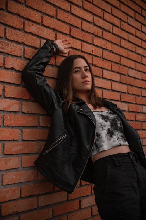 Woman in Black Leather Jacket Leaning Against a Brick Wall