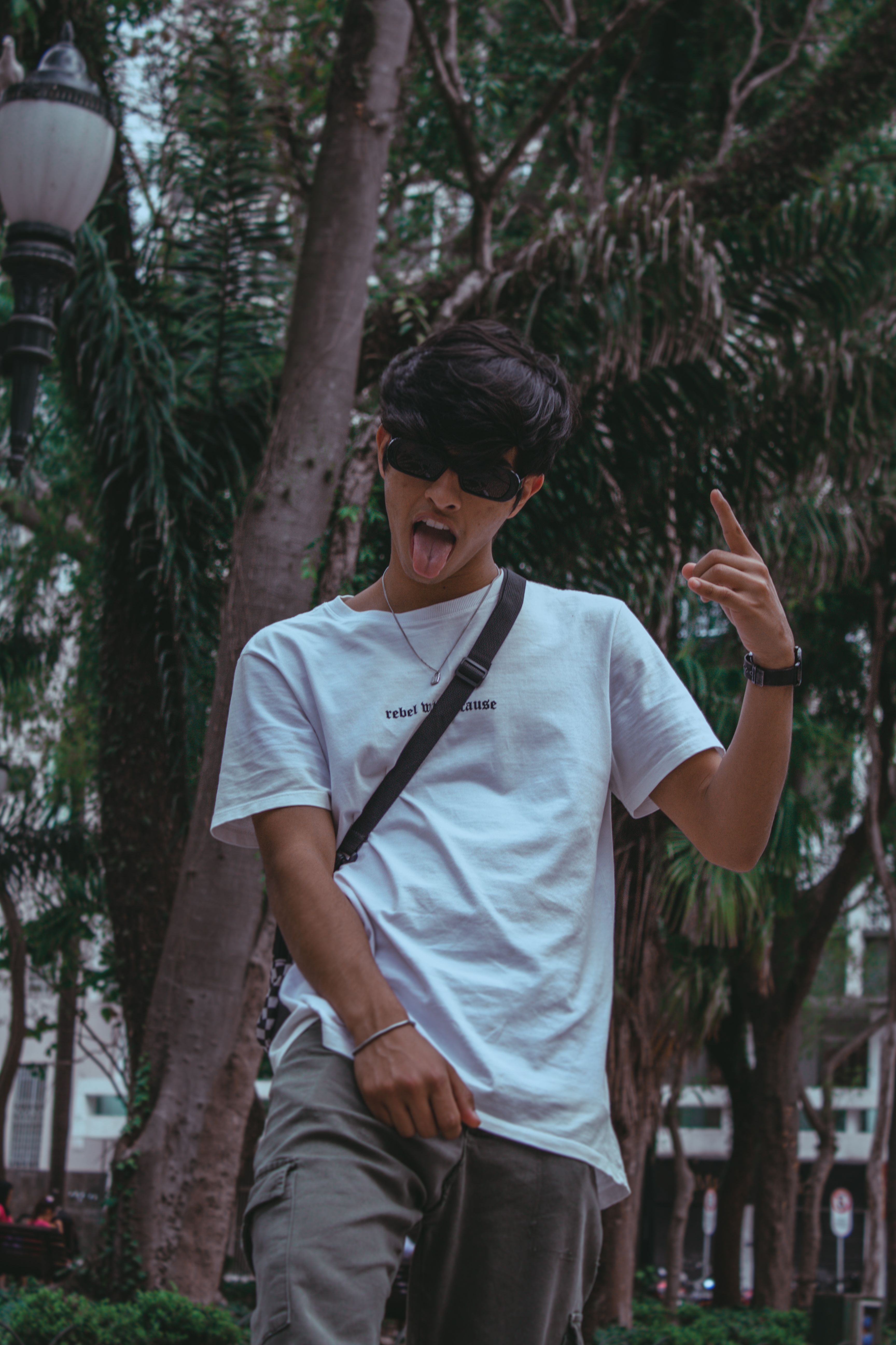 Stylish young adult making a playful hand gesture in a lush Curitiba park.