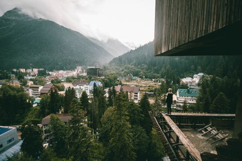 Free A person stands on a wooden platform, overlooking a scenic mountain town with forests and buildings. Stock Photo