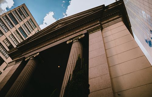 Free A low-angle view of classic columns against modern skyscraper reflecting the sky. Stock Photo
