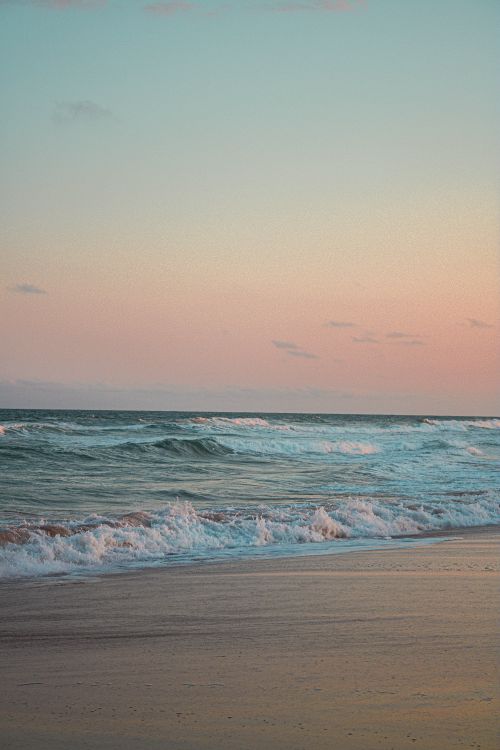 Free Peaceful beach scene during twilight with pastel sky and gentle waves. Stock Photo