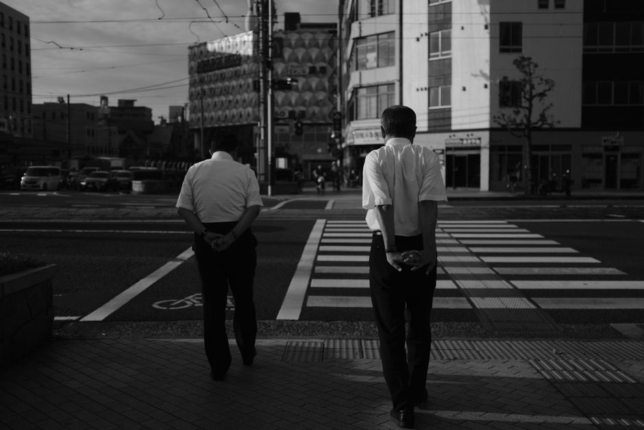 Black and white view of two men crossing at a Matsuyama intersection in Japan.