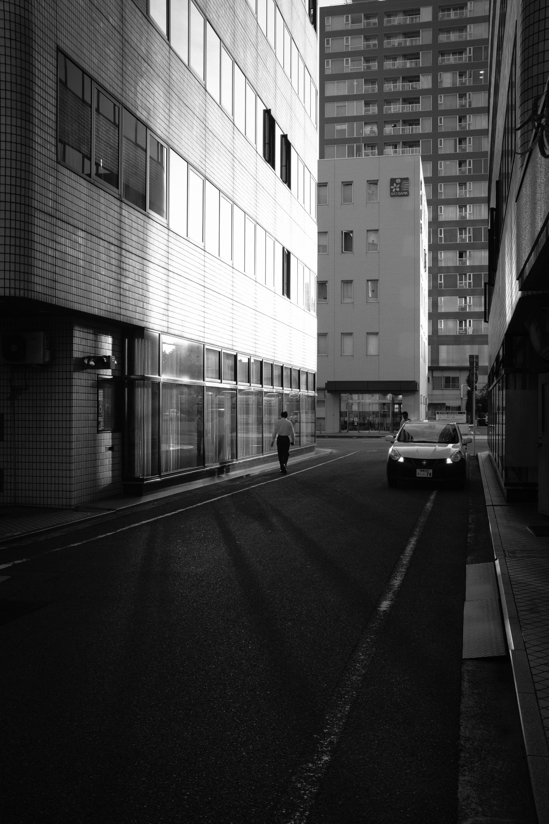 Black and white street scene with a pedestrian and parked car in Japan