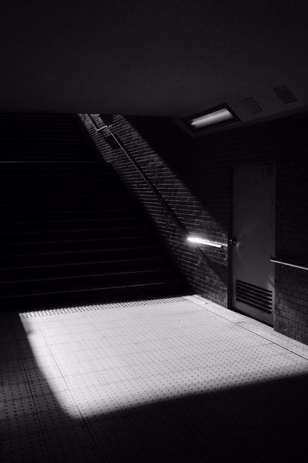 A dramatic play of light and shadows in a monochrome underground stairwell creates a moody atmosphere.