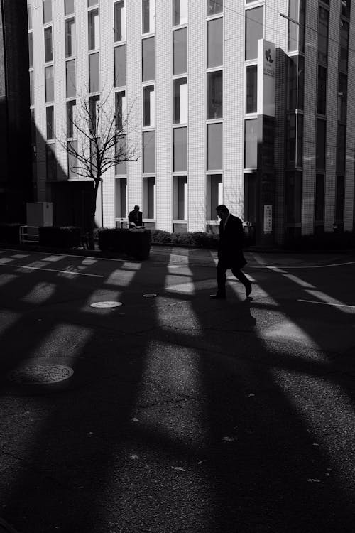 Black and White Photo of a Man Walking on the Road near a Building