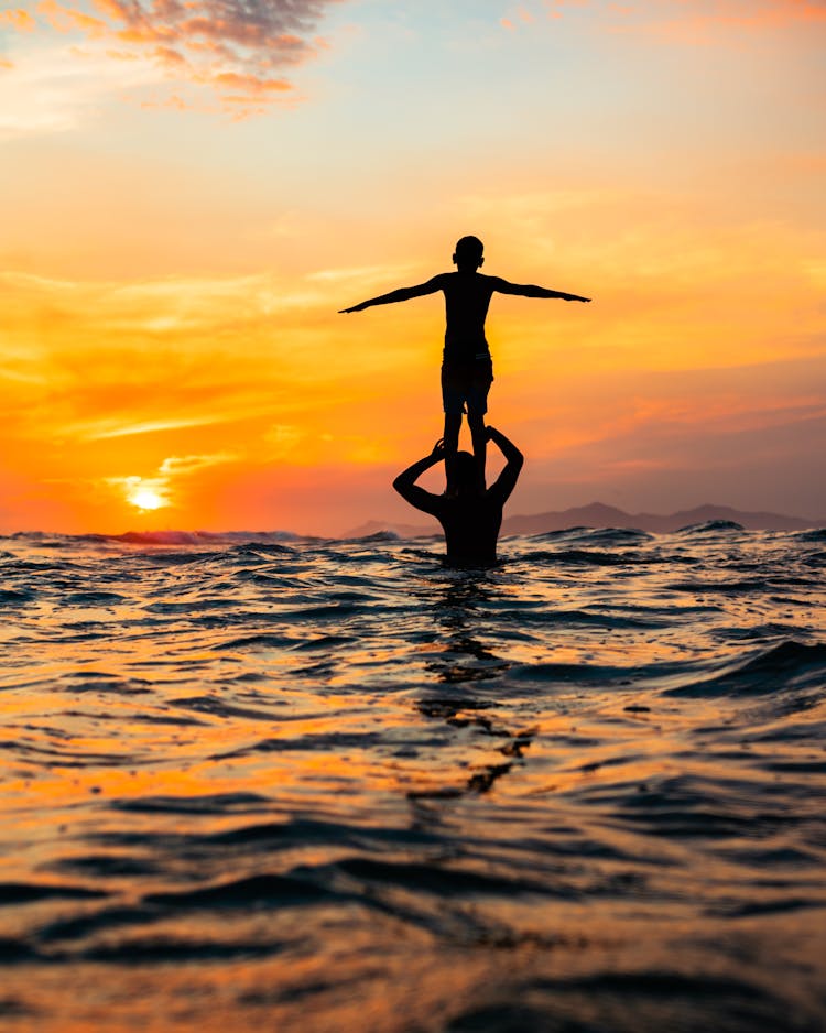 Silhouette Of A Child Standing On The Shoulders Of A Person While In The Sea