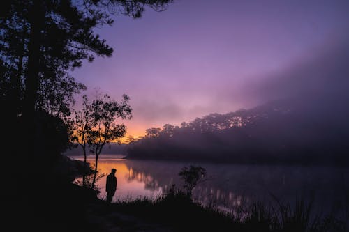 Free Silhouette of a Man Standing by the River Stock Photo