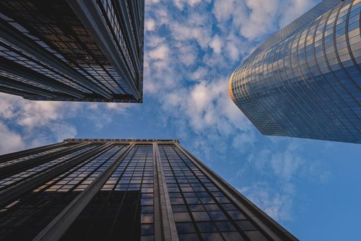 Low angle view of modern skyscrapers reaching up to a partly cloudy blue sky.
