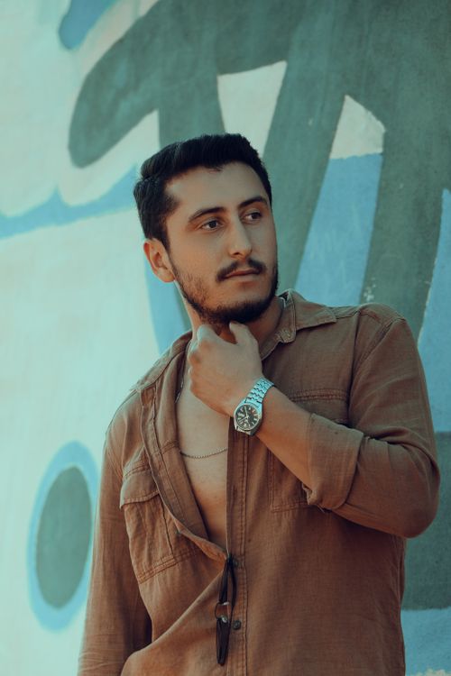 Free Young man with a beard posing confidently outdoors with a stylish watch and brown shirt. Stock Photo