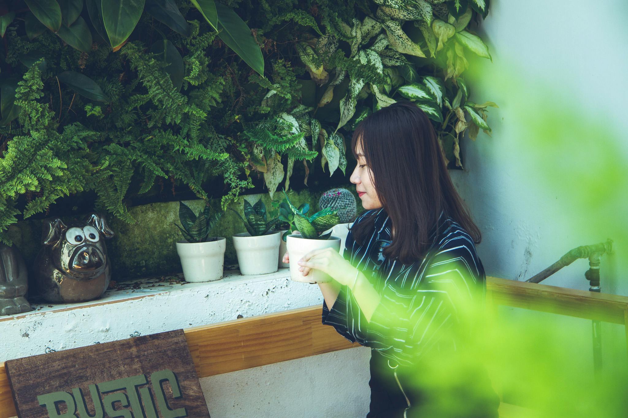 woman holding white clay pot with green plant sitting near white painted wall