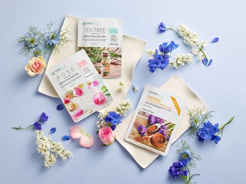 Free Beautiful floral arrangement with skincare face mask packaging on a blue background. Stock Photo