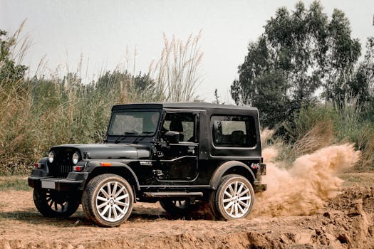 Dynamic photo of a Black Mahindra Thar SUV kicking up dust while off-roading in an outdoor setting.